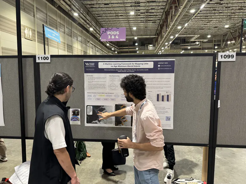 Mohammad Salmani pointing at the satellite-image panels of his machine-learning poster at board 1100 while a visitor listens.
